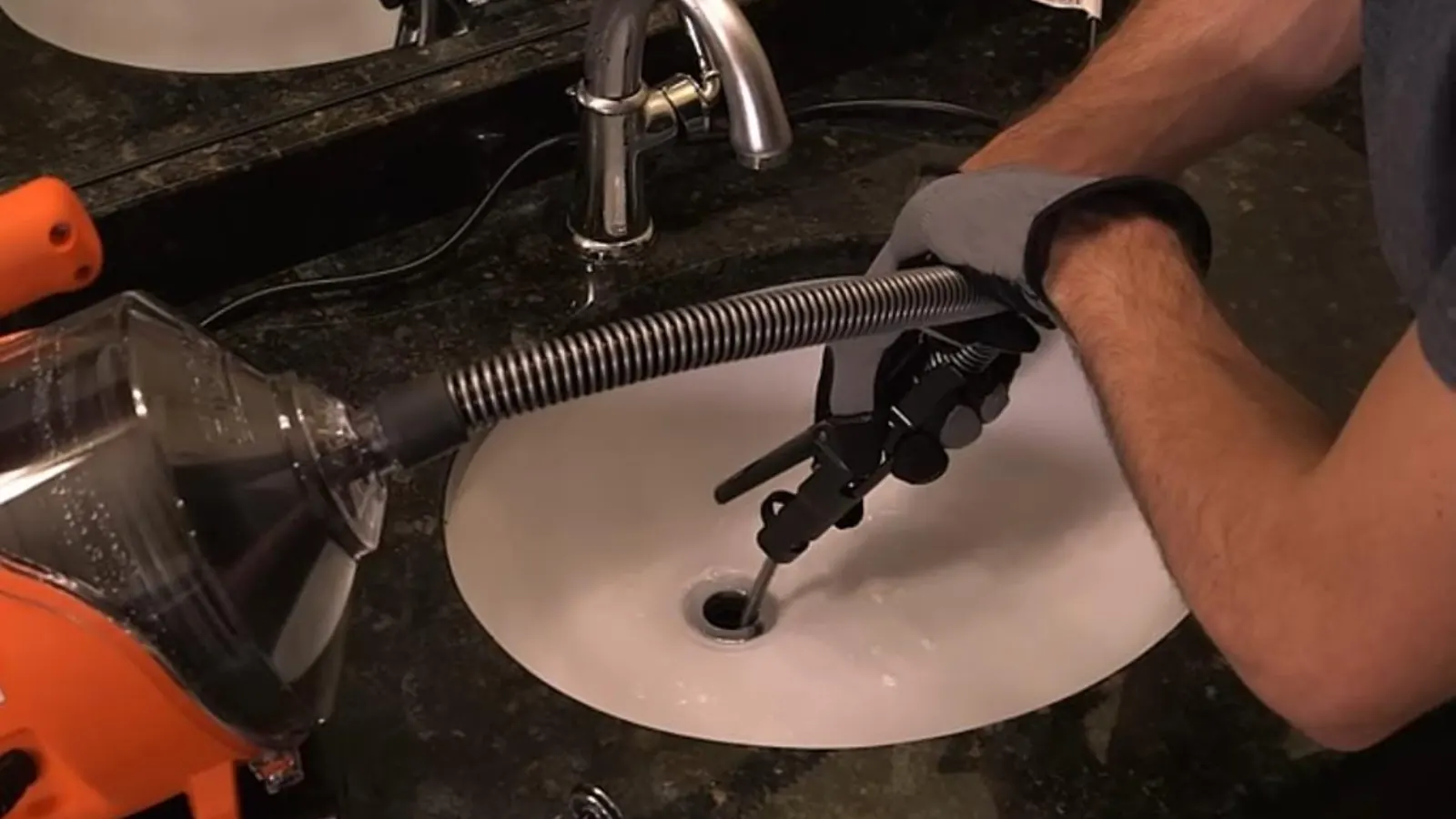 Gloved hands feeding a drain machine cable into a kitchen sink drain
