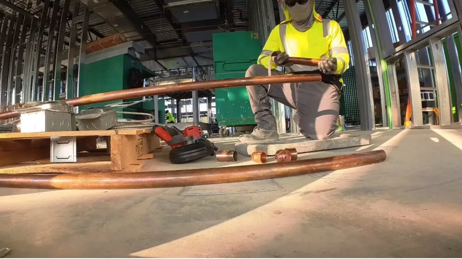 Plumber in a high-visibility vest installing copper piping at a construction site