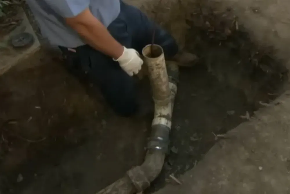 Plumber kneeling in an excavated trench working on a buried sewer pipe