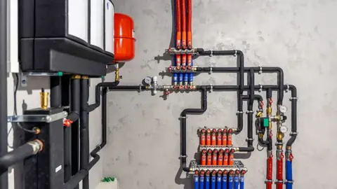 Hydronic boiler manifold with red and blue supply and return piping mounted on a wall