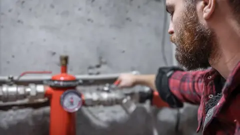Plumber checking a pressure gauge and valve on a water supply line in a basement