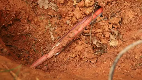 Exposed copper water line in a trench dug into red clay soil