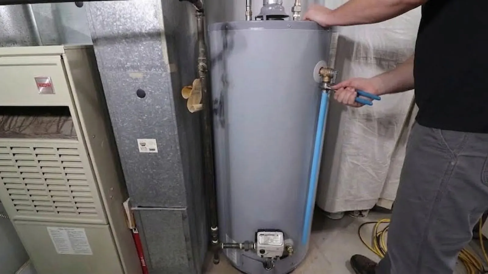 Plumber working on a tank water heater next to a furnace, connecting the water lines in a utility room
